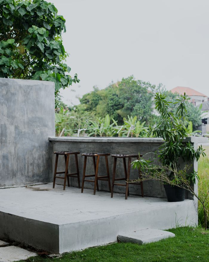 Minimalist outdoor patio with high stools and green plants.